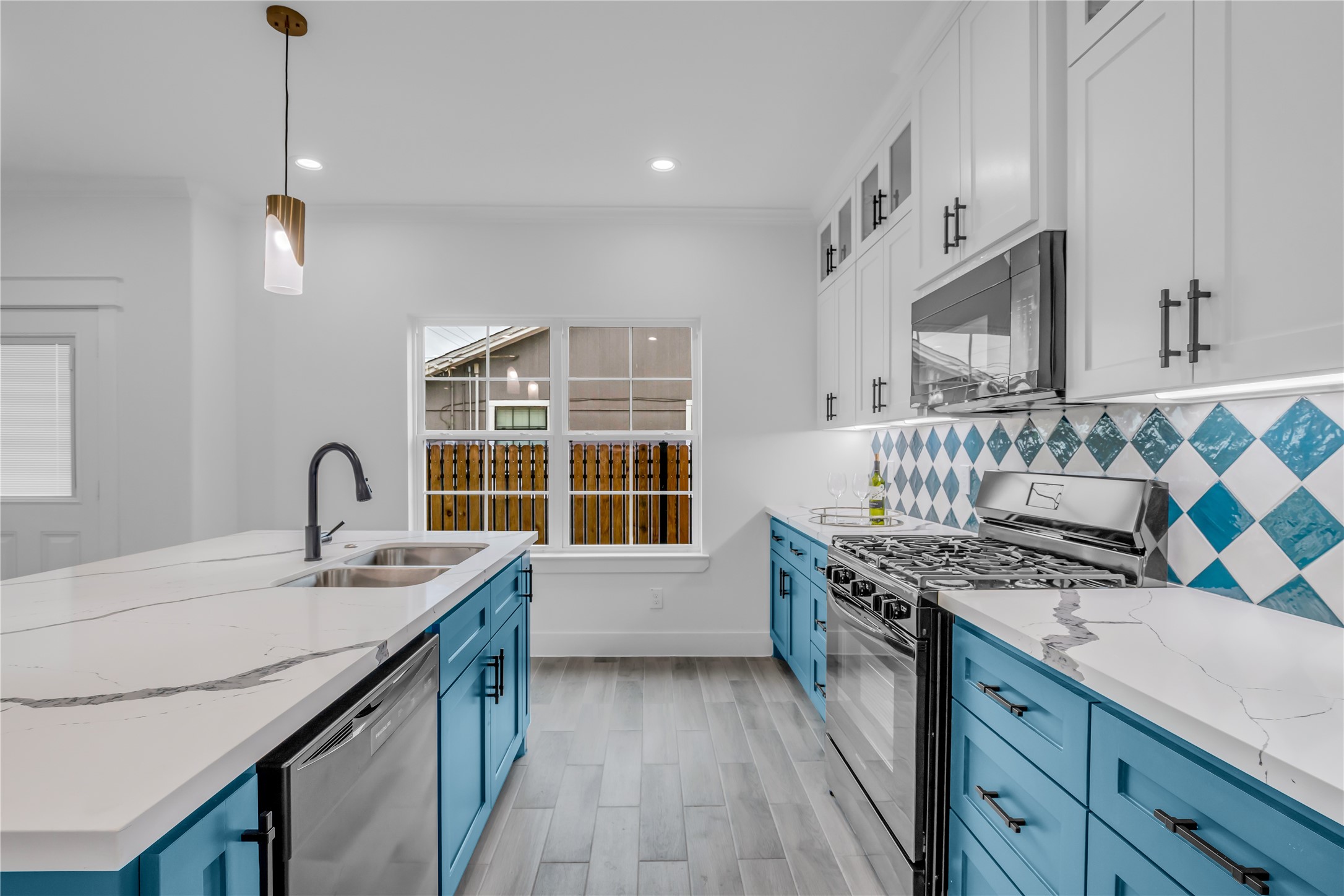 3168 Golfcrest Houston, TX 77087 - Photo 11 of 30 This kitchen boasts a modern flair with its striking blue cabinetry, sleek stainless steel appliances, and elegant marble countertops, all illuminated by stylish pendant lighting for a bright, inviting atmosphere.