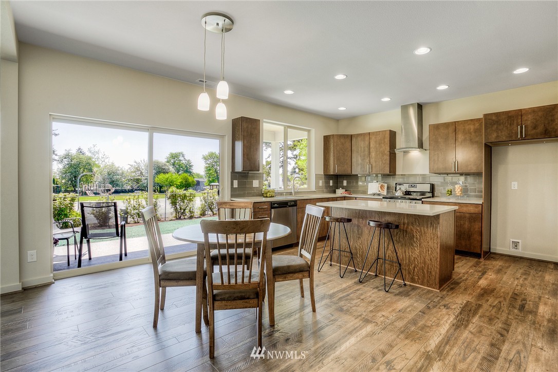 719 Southwest Langston Road Renton, WA 98057 - Photo 5 of 25 a kitchen with stainless steel appliances kitchen island granite countertop a dining table chairs and wooden floor
