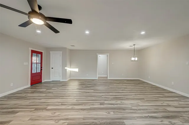 a view of an empty room with wooden floor and a ceiling fan