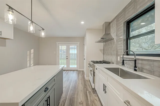 a large kitchen with granite countertop a sink dishwasher a stove and white cabinets with wooden floor