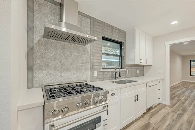 a kitchen with a sink dishwasher a stove and white cabinets with wooden floor
