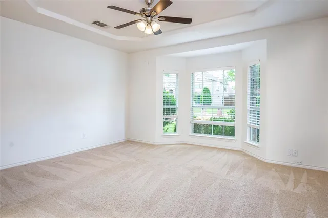 an empty room with chandelier fan and windows
