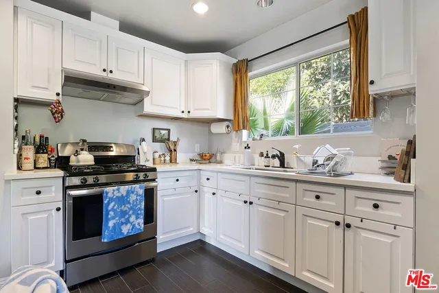 a kitchen with stainless steel appliances granite countertop white cabinets a stove a sink and a window