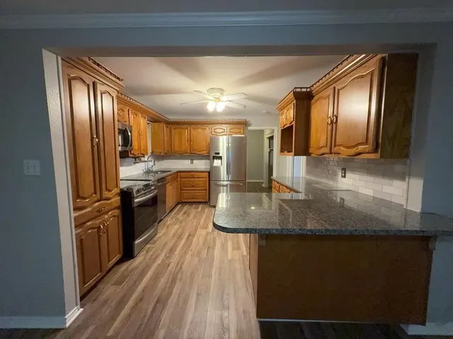 a kitchen with stainless steel appliances granite countertop a refrigerator a stove and a sink with wooden floors