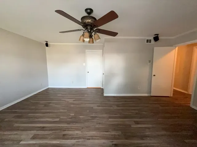 a view of an empty room with wooden floor and ceiling fan