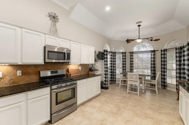 a kitchen with stainless steel appliances granite countertop a stove top oven a sink a dining table and chairs