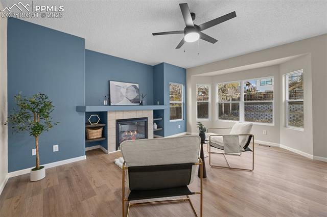 5428 Rondo Way Colorado Springs, CO 80911 - Photo 14 of 43 Living room featuring a fireplace, a textured ceiling, light wood-style floors, and ceiling fan