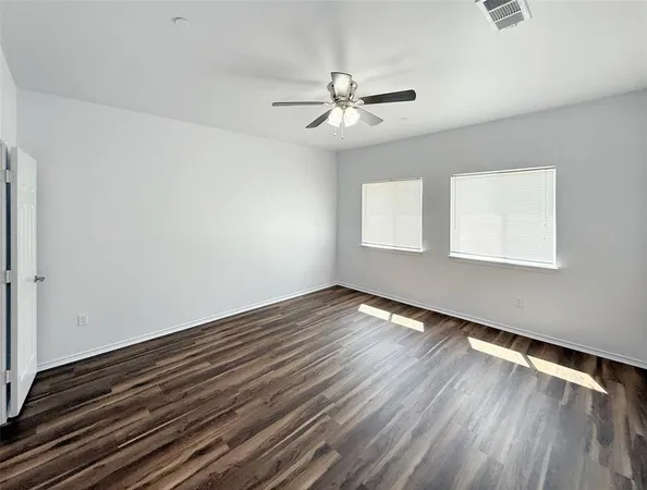 an empty room with wooden floor chandelier fan and windows