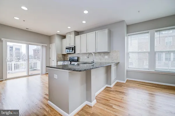 a kitchen with granite countertop a stove a sink a refrigerator and white cabinets with wooden floor