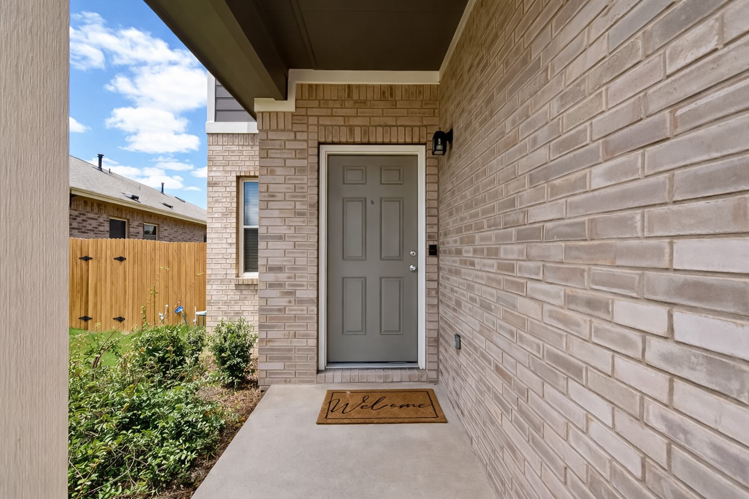 940 Paddock Lane Georgetown, TX 78626 - Photo 4 of 32 Brick exterior featuring a covered porch entry, a gray paneled door with polished hardware, a contrasting trim, and mature landscaping