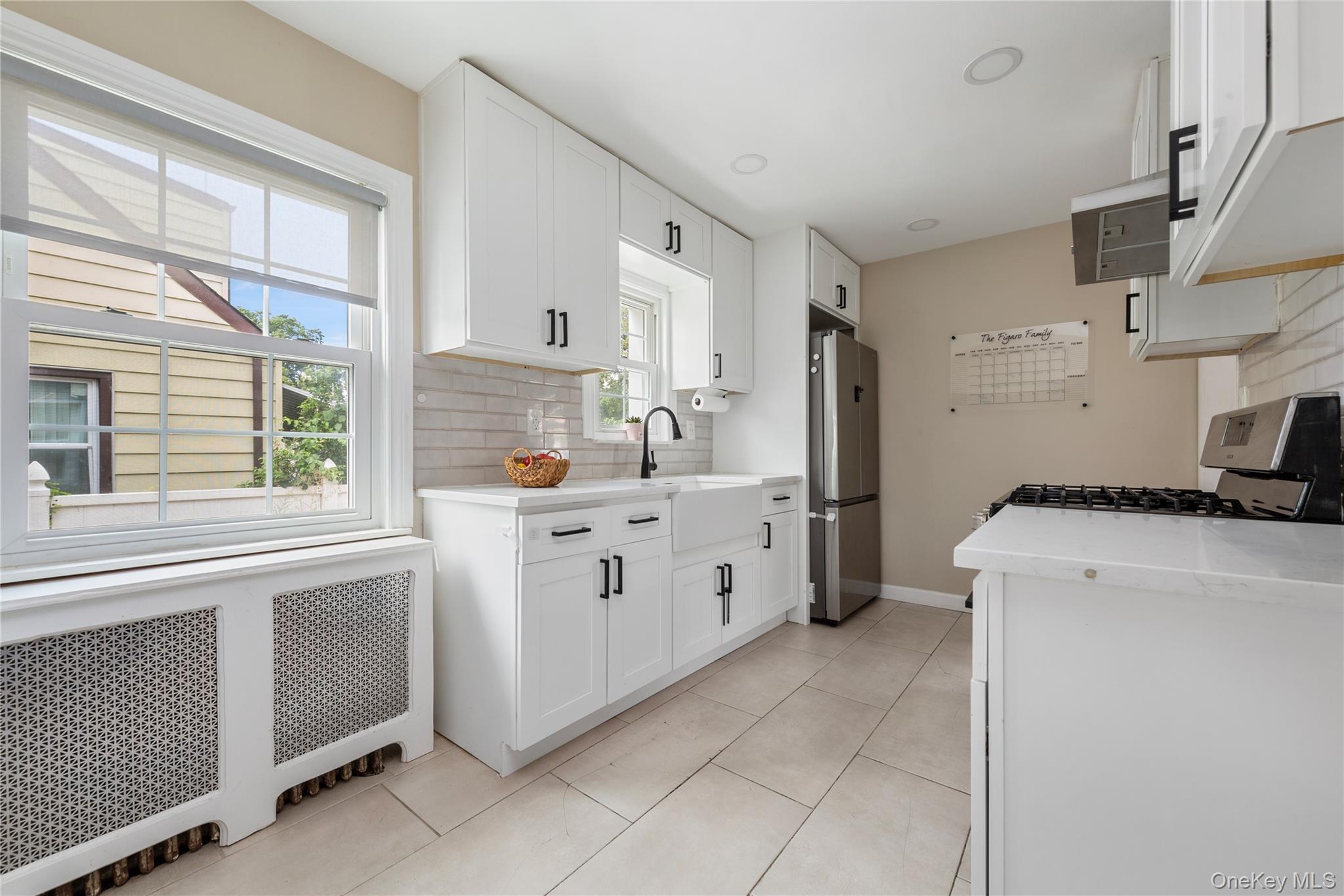11 Dewitt Street Valley Stream, NY 11580 - Photo 7 of 21 Kitchen with radiator heating unit, decorative backsplash, white cabinetry, appliances with stainless steel finishes, and light stone countertops