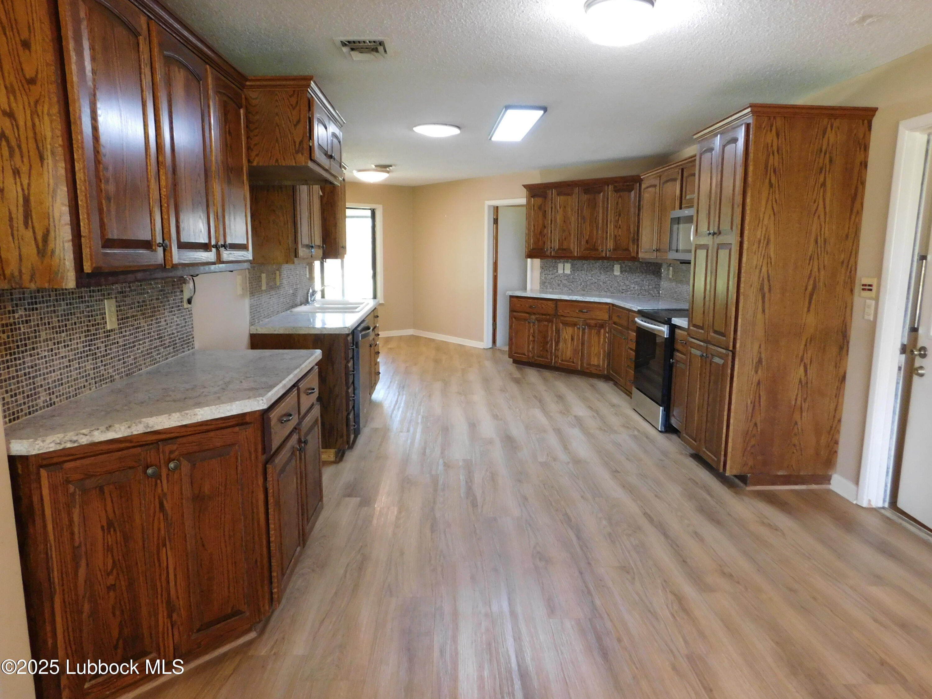 1925 Highway 70 Muleshoe, TX 79347 - Photo 12 of 49 a kitchen with stainless steel appliances granite countertop a refrigerator a sink dishwasher and wooden cabinets with wooden floor