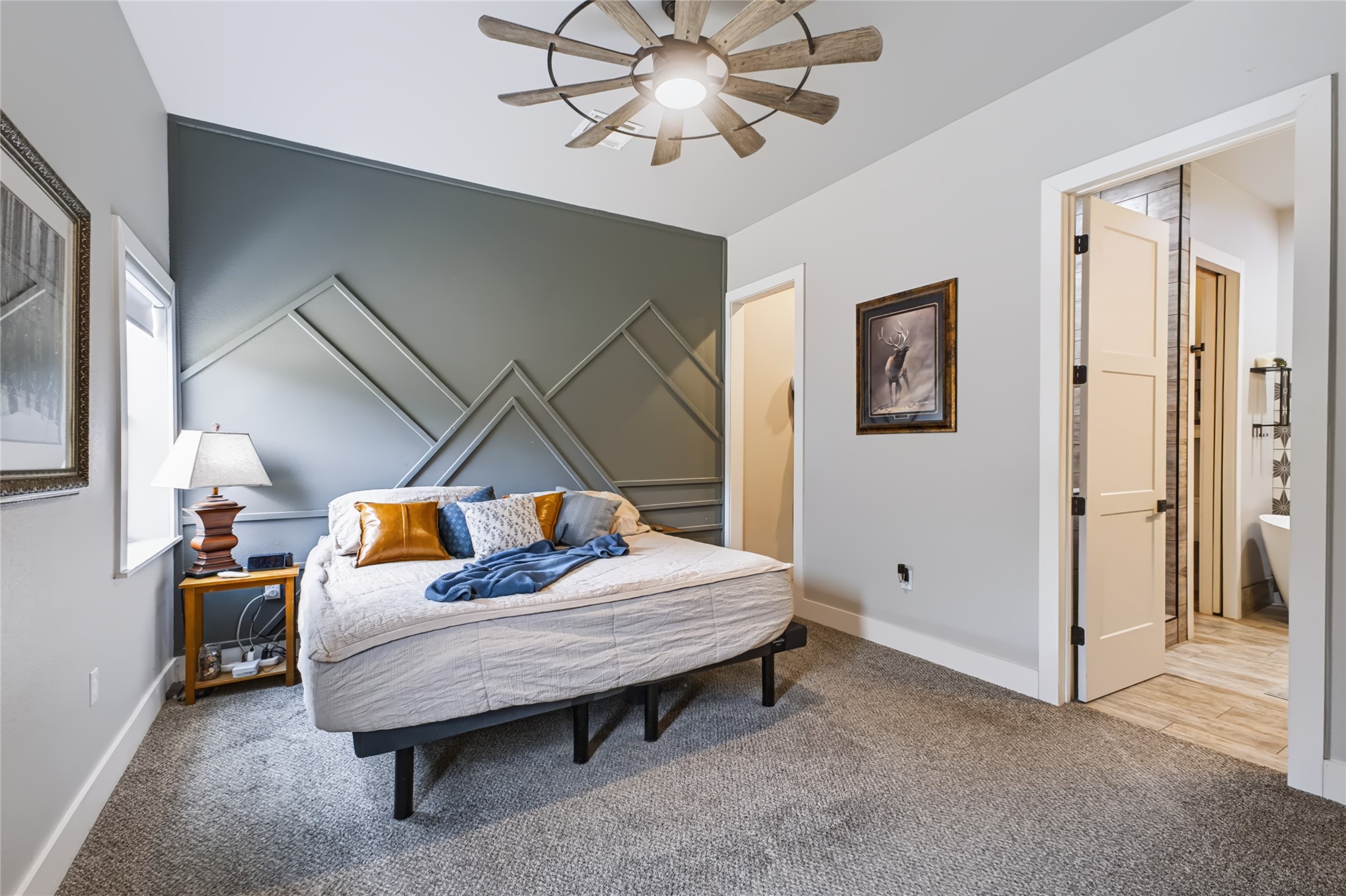 3607 South Half Bank Road Atoka, OK 74525 - Photo 18 of 82 Feature wall with geometric molding, ceiling fan with wood-finish blades, light gray walls, window with white trim, and a door leading to a bathroom with tile-look flooring