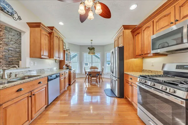 a kitchen with stainless steel appliances granite countertop a stove top oven a sink dishwasher a dining table and chairs with wooden floor