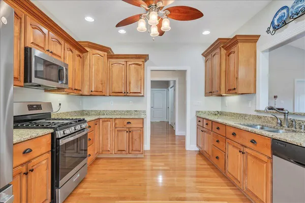 a kitchen with stainless steel appliances granite countertop a stove top oven a sink dishwasher and white cabinets with wooden floor