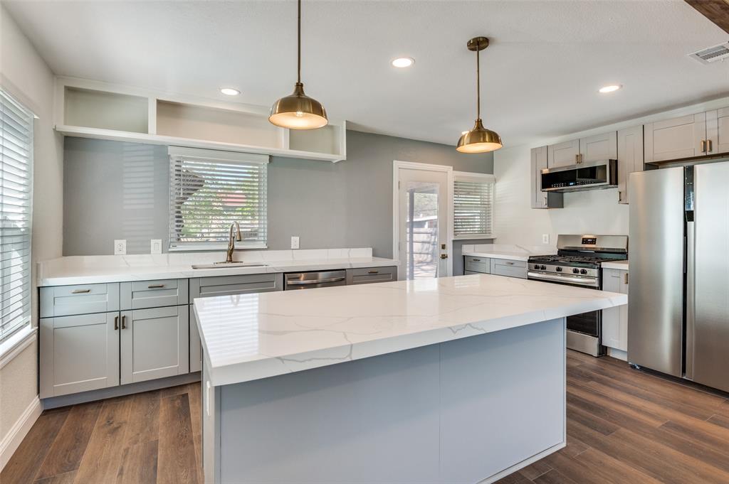 Kitchen with stainless steel appliances, dark wood finished floors, light stone countertops, pendant lighting, and gray cabinets