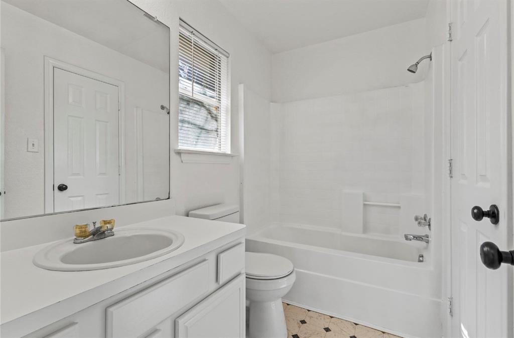 5169 East Rim Road Dallas, TX 75211 - Photo 12 of 19 Bathroom featuring a white vanity with an integrated sink, an overhead mirror, a toilet, a bathtub with a shower, and patterned flooring