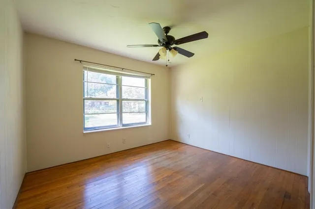 an empty room with wooden floor fan and windows