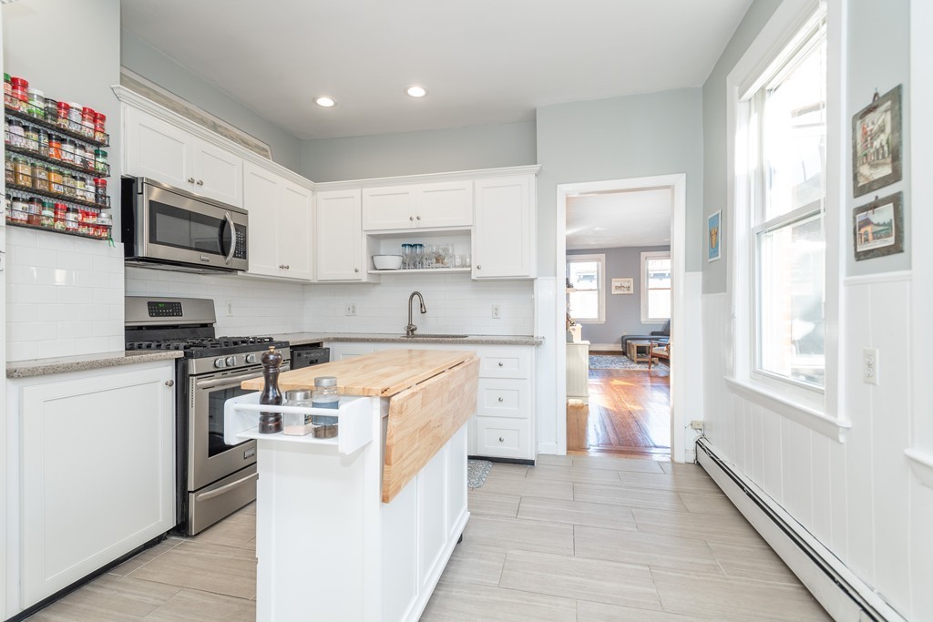 23-23A Sullivan Street, Unit 3 Boston, MA 02129 - Photo 3 of 8 a large kitchen with stainless steel appliances granite countertop a stove top oven a sink a refrigerator and white cabinets with wooden floor