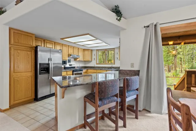 a kitchen with stainless steel appliances a refrigerator a stove a dining table and chairs with the outer view