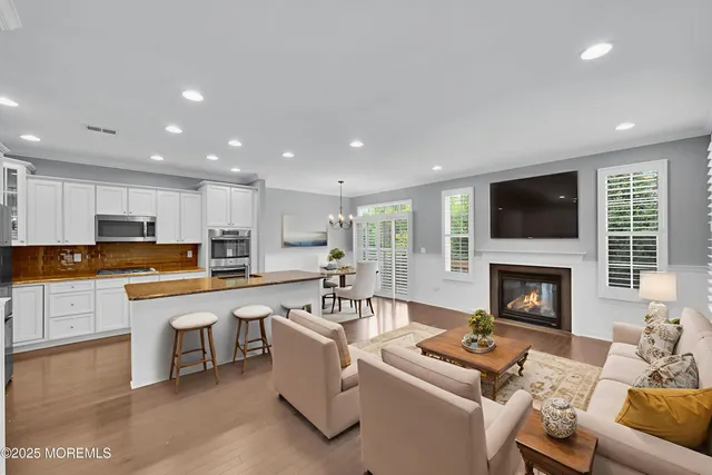 a living room with stainless steel appliances furniture a fireplace a flat screen tv and a kitchen view