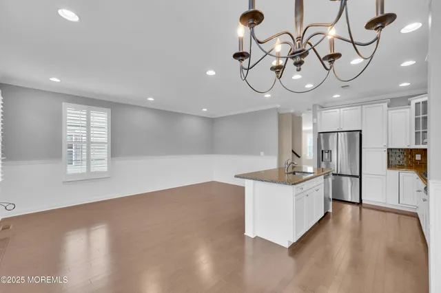 a kitchen with stainless steel appliances granite countertop a sink a stove oven a refrigerator with white cabinets and wooden floor