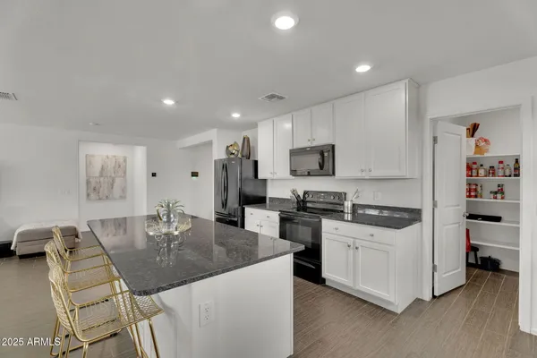 a kitchen with stainless steel appliances granite countertop a refrigerator a stove a sink a microwave a dining table and chairs with wooden floor