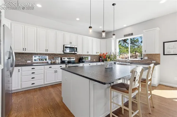 a kitchen with stainless steel appliances granite countertop a sink a stove a refrigerator and island with wooden floor