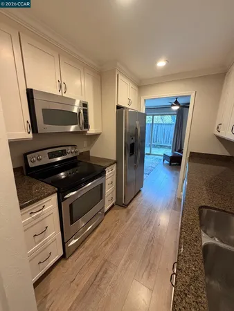 a kitchen with stainless steel appliances granite countertop a refrigerator a sink dishwasher a stove and white countertops with wooden floor