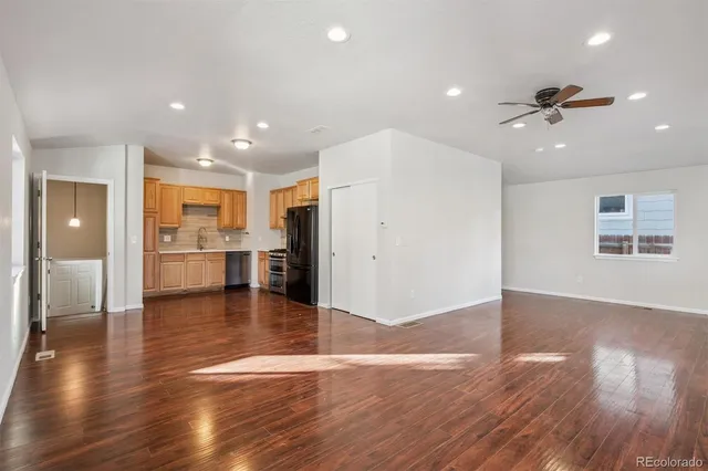 a view of an empty room and kitchen with wooden floor