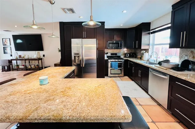 a kitchen with stainless steel appliances kitchen island granite countertop a sink refrigerator and microwave