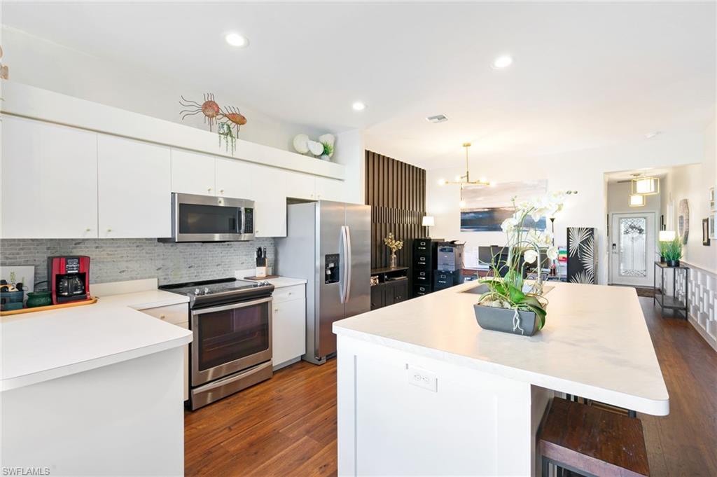 21445 Knighton Run Estero, FL 33928 - Photo 11 of 48 a kitchen with stainless steel appliances kitchen island granite countertop a stove a sink a refrigerator a microwave oven with white cabinets and wooden floor