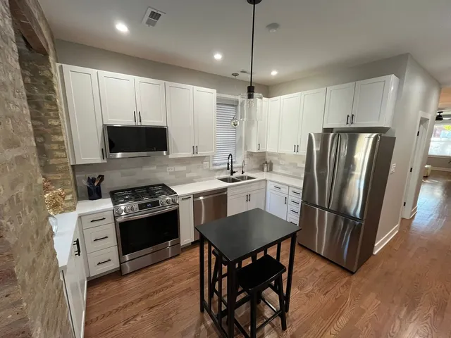 a kitchen with stainless steel appliances a stove a sink dishwasher a refrigerator white cabinets and wooden floor
