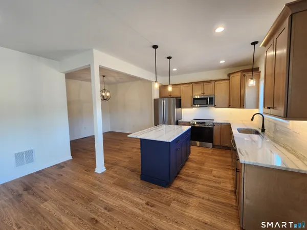 a living room with stainless steel appliances kitchen island granite countertop wooden floor and a refrigerator