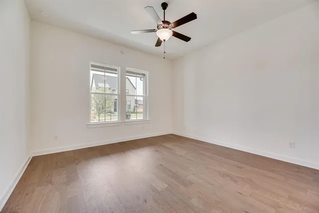 an empty room with wooden floor ceiling fan and windows