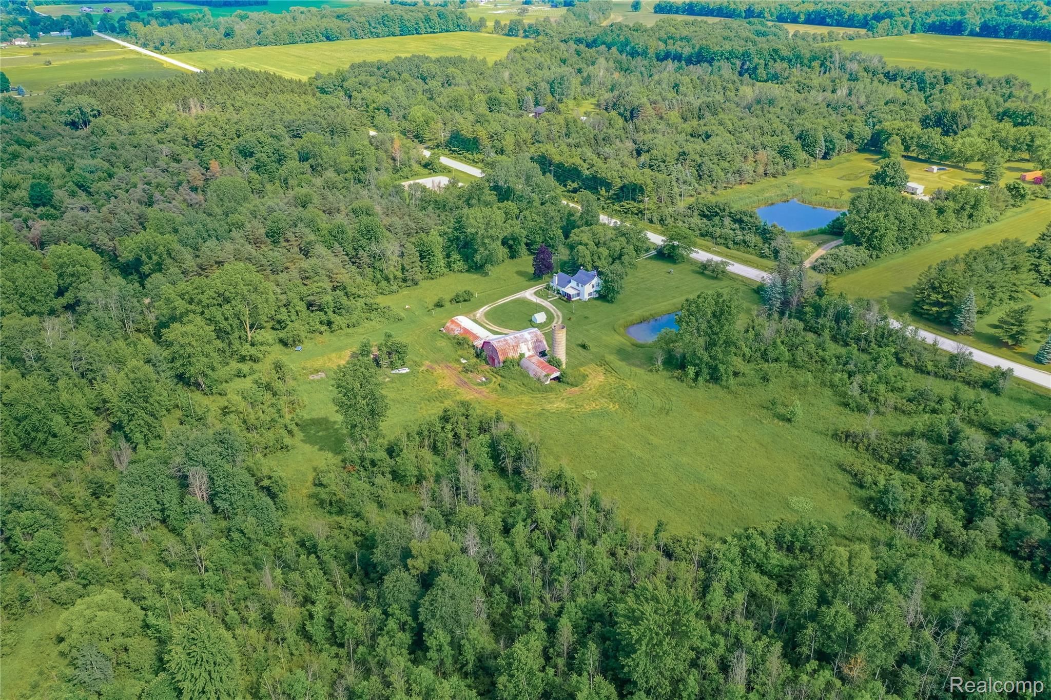 8384 Imlay City Road Avoca, MI 48006 - Photo 5 of 39 Expansive property featuring a white residential structure, multiple outbuildings, two visible ponds, and a mix of cleared land and mature woodlands