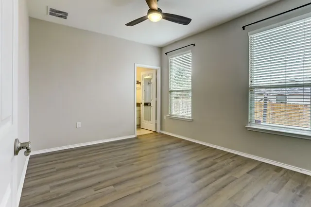 an empty room with wooden floor chandelier fan and windows