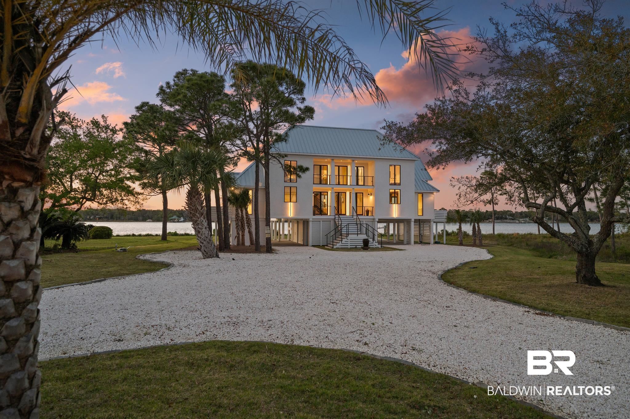 33349 River Road Orange Beach, AL 36561 - Photo 55 of 61 Contemporary waterfront residence featuring a light-colored metal roof, multiple balconies, a white exterior, and a spacious gravel driveway