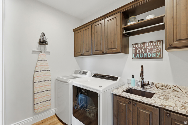 10676 Urban Rdg Cove South Jordan, UT 84095 - Photo 25 of 48 Laundry room featuring wood-finish cabinetry, a stone countertop, an undermount sink with a dark bronze faucet, and wood-finish flooring