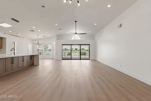 a view of an empty room with wooden floor kitchen view and a window
