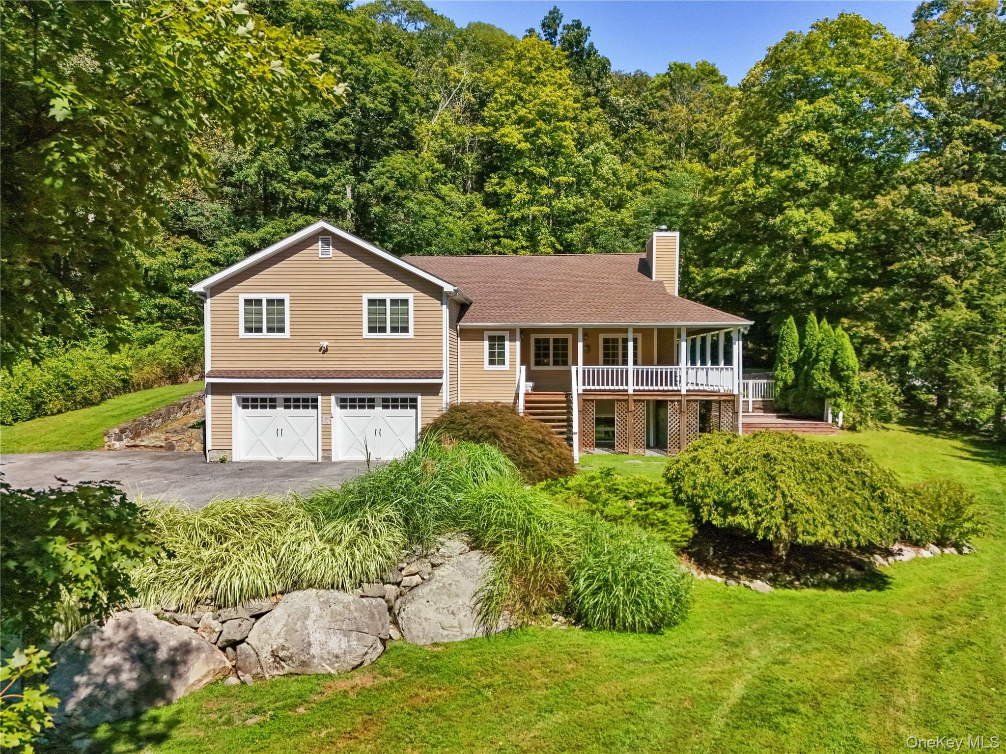 Split level home featuring asphalt driveway, a chimney, a porch, and a front lawn