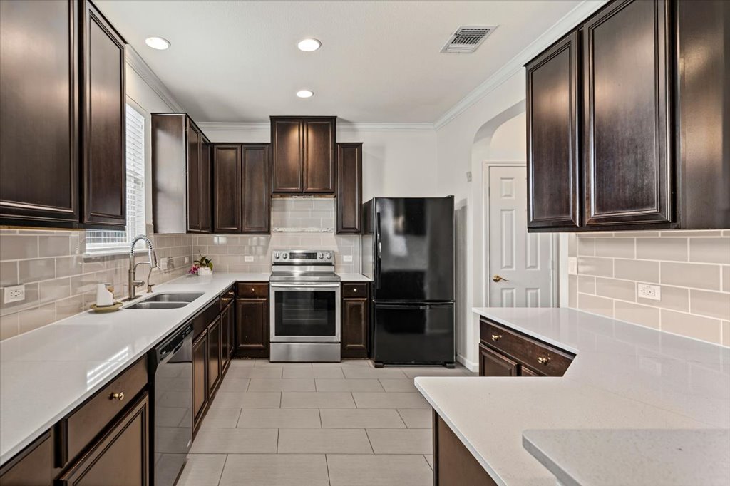 11229 Kirkland Hill Path Austin, TX 78754 - Photo 7 of 15 Kitchen featuring black appliances, crown molding, dark brown cabinetry, light stone countertops, and tasteful backsplash