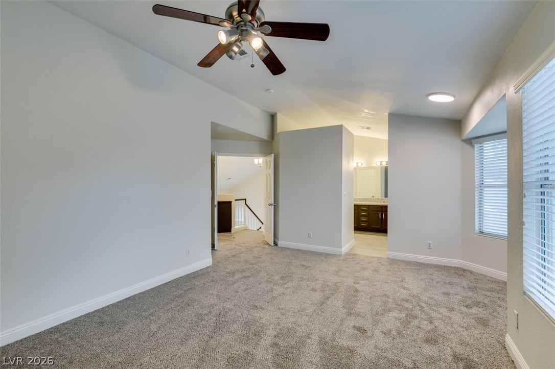 1738 Toltec Circle Henderson, NV 89014 - Photo 34 of 46 A comfortable bedroom features carpeted floors, a ceiling fan, and access to a primary bathroom.