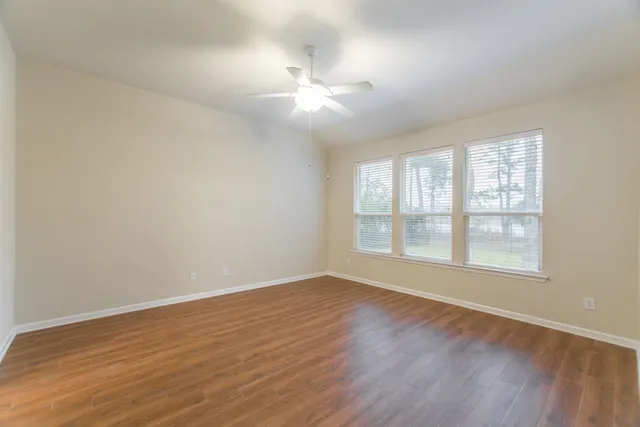 an empty room with wooden floor fan and windows