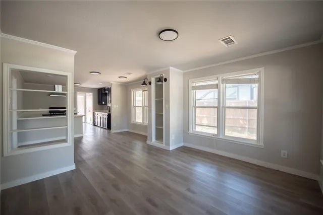 an empty room with wooden floor kitchen view and windows