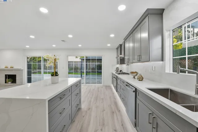 a large kitchen with stainless steel appliances a sink dishwasher a stove and a large window with wooden floor