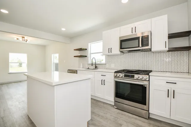a hall with kitchen island white cabinets and wooden floor
