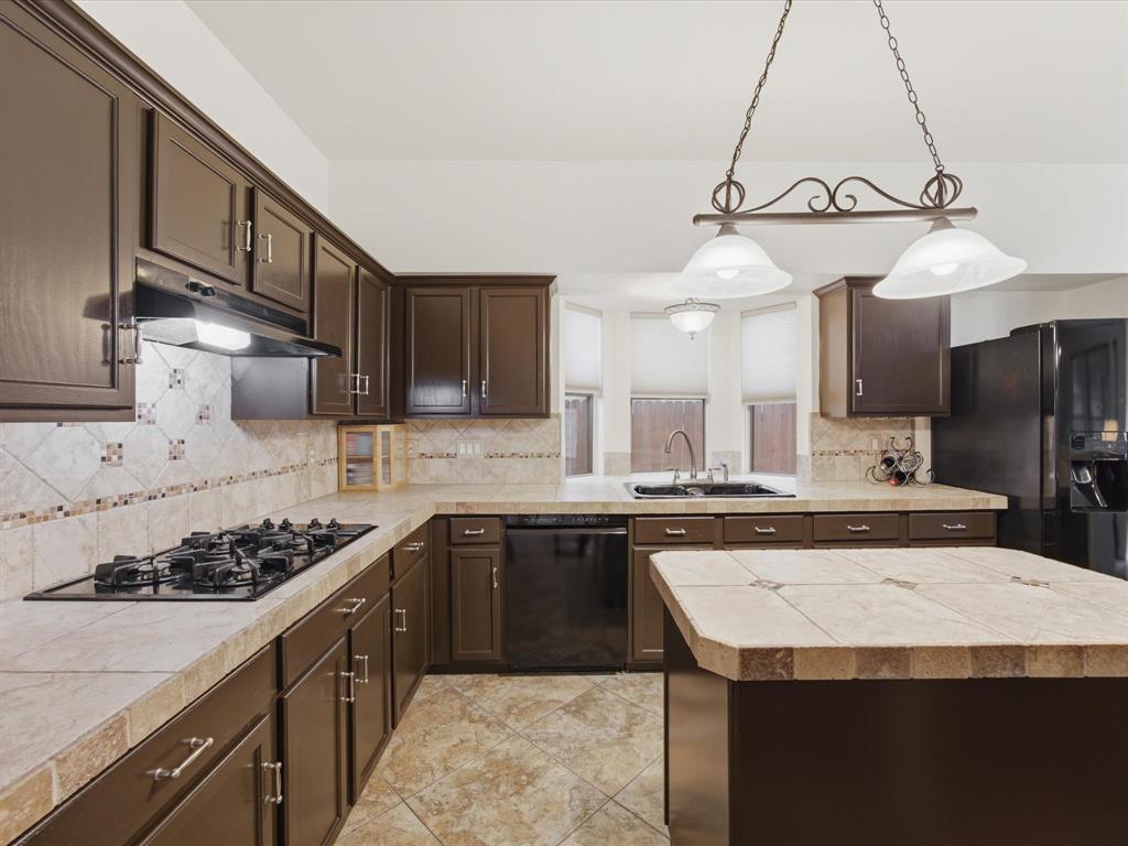 4008 Falcon Ridge Drive Haltom City, TX 76137 - Photo 12 of 40 Kitchen featuring dark wood-finish cabinetry, tile countertops, a gas cooktop, and a matching tile backsplash