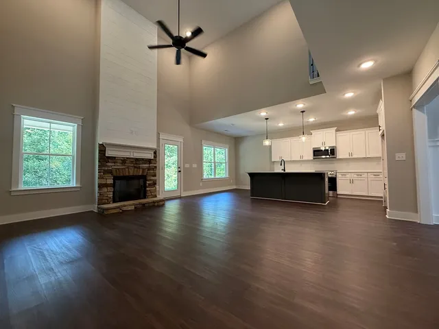 an empty room with wooden floor fire place and kitchen view