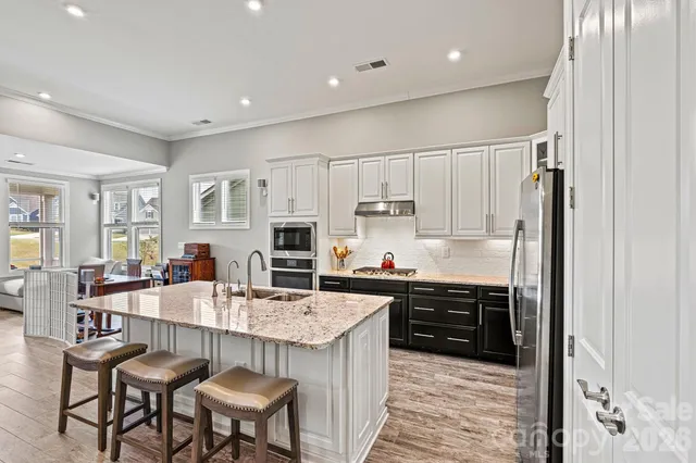 a kitchen with stainless steel appliances a sink a stove a refrigerator cabinets and chairs